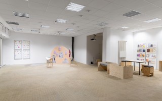 Im Zentrum des Raumausschnitts ist eine Nische, die weniger hell beleuchtet ist als der Rest des Ausstellungsraumes. Dort stehen zwei Hocker und es wird die Videoarbeit „Notes from the Underlands“ (2019) von Romily Alice Walden an die Wand projiziert. Es