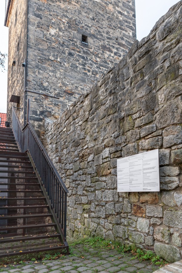 Zum Eingang des Kunstvereins führt links eine Stahltreppe zur Tür des alten Turms, der im Hintergrund des Bildes ausschnitthaft zu sehen ist. Der Turm und die daran anschließende Mauer sind aus großen groben Steinen. Die Mauer führt in der Mitte des Bilde